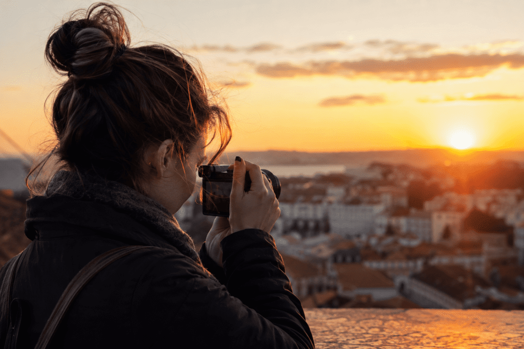 Une personne en extérieur, appareil photo à la main, en train de photographier un paysage urbain en fin de journée.